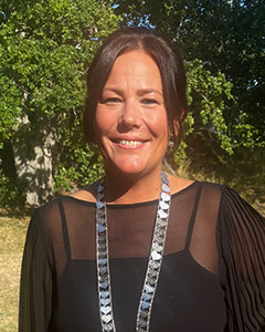 Kvinna med mörkbrunt hår i hästsvans ler med halvöppen mun. Hon har en svart klänning och ett långt silvrigt halsband.