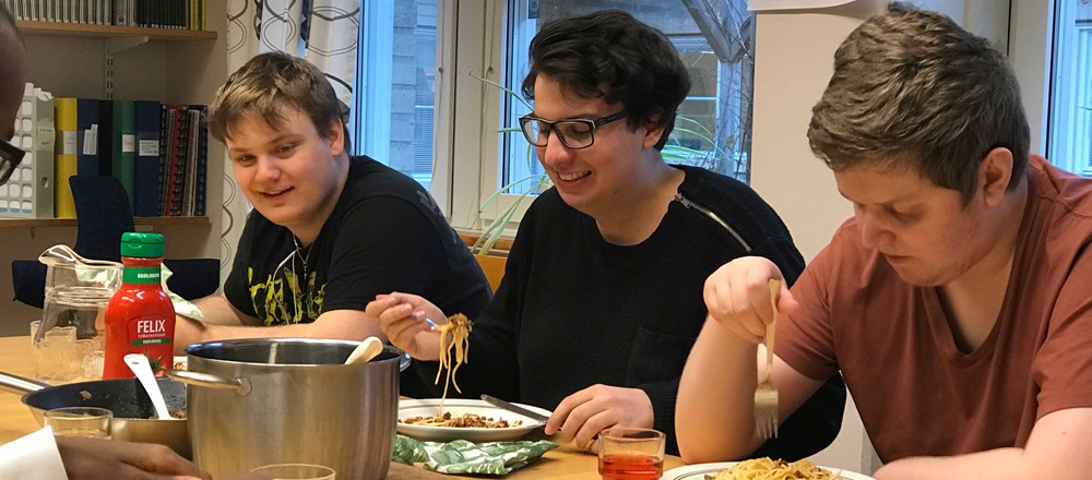 Tre glada unga män äter spagetti och köttfärssås tillsammans.