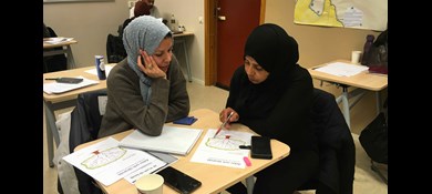 Två kvinnor sitter vid bord och studerar i klassrum.