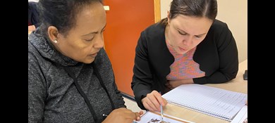 Två kvinnor sitter vid bord i klassrum och gör uppgift med papper och penna.