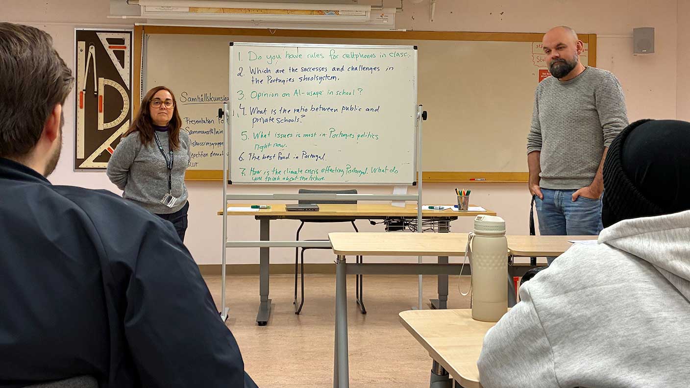 Kvinna och man står vid whiteboard i klassrum och tittar mot två sittande kursdeltagare.