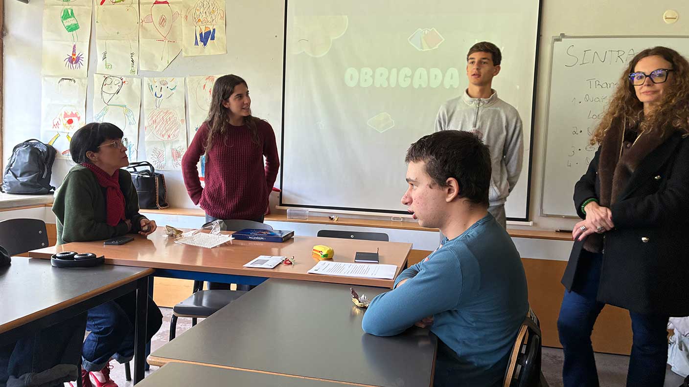 Fyra unga personer i löassrum framför projektorduk. Till höger lärare som följer en presentation.