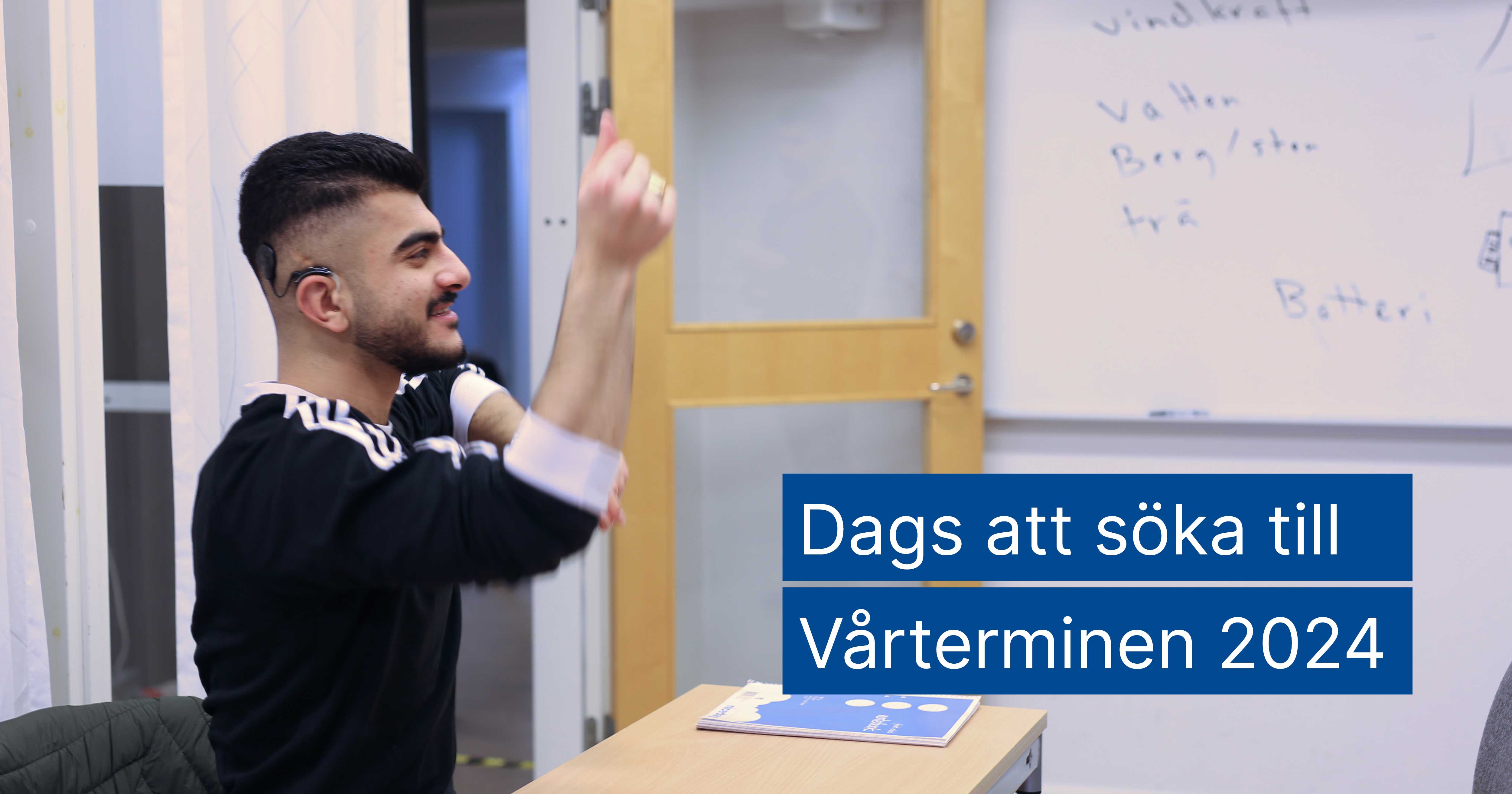 Ung man med svart hår och hörapparat räcker upp handen i klassrummet.