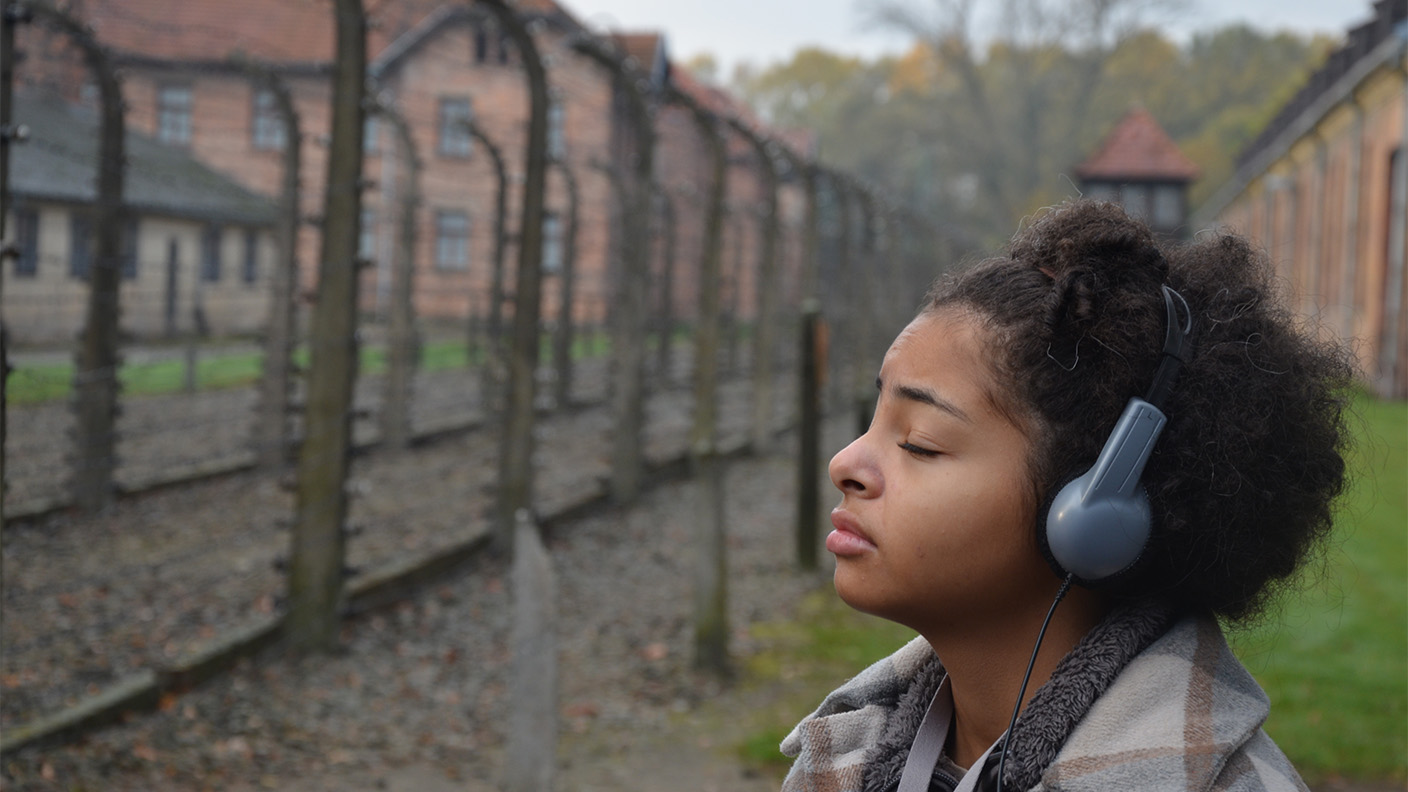 Ung kvinna med headset blundar med bekymrad min framför högt metallstaket med taggtrådsstängsel.